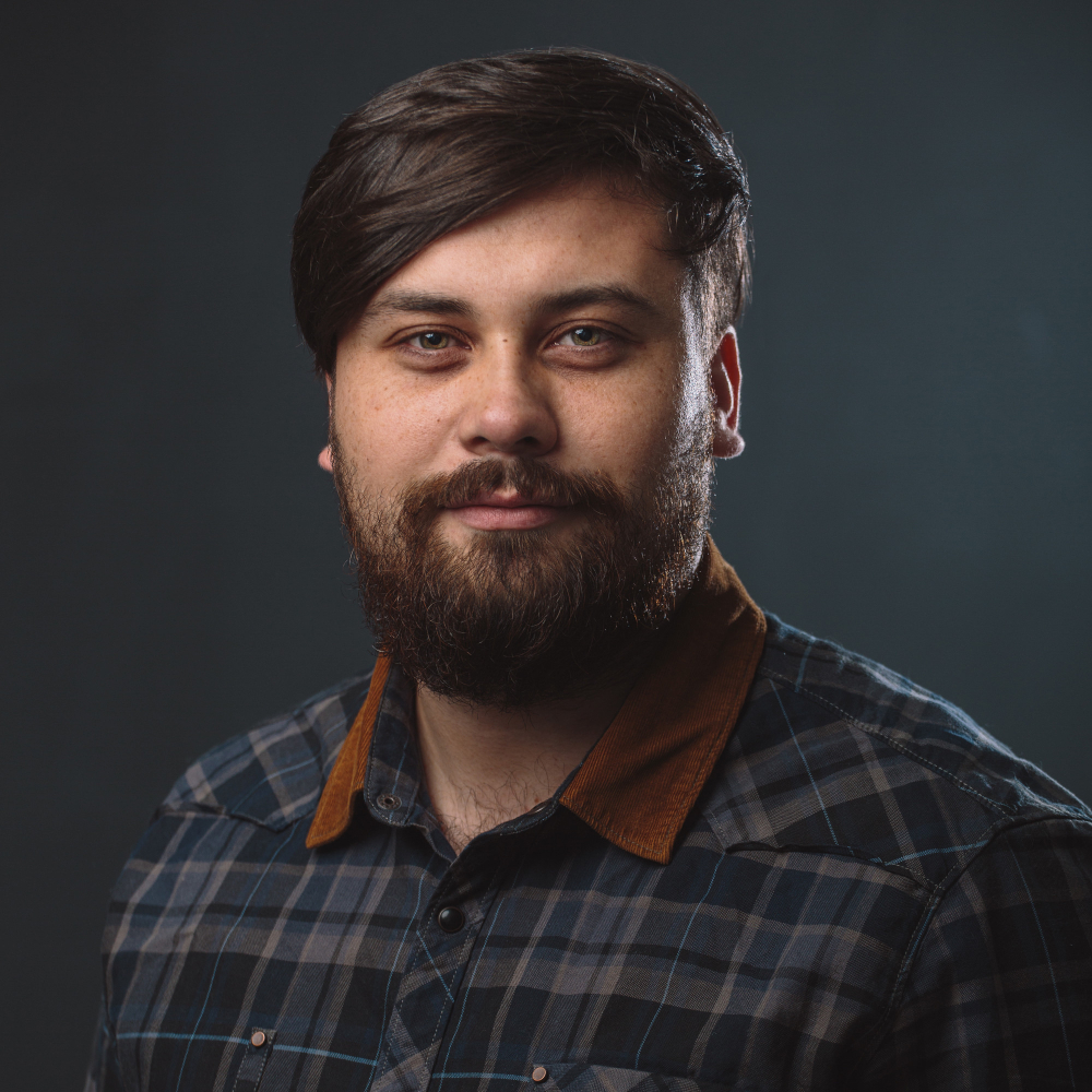 Person with dark hair and beard wearing a checkered shirt.
