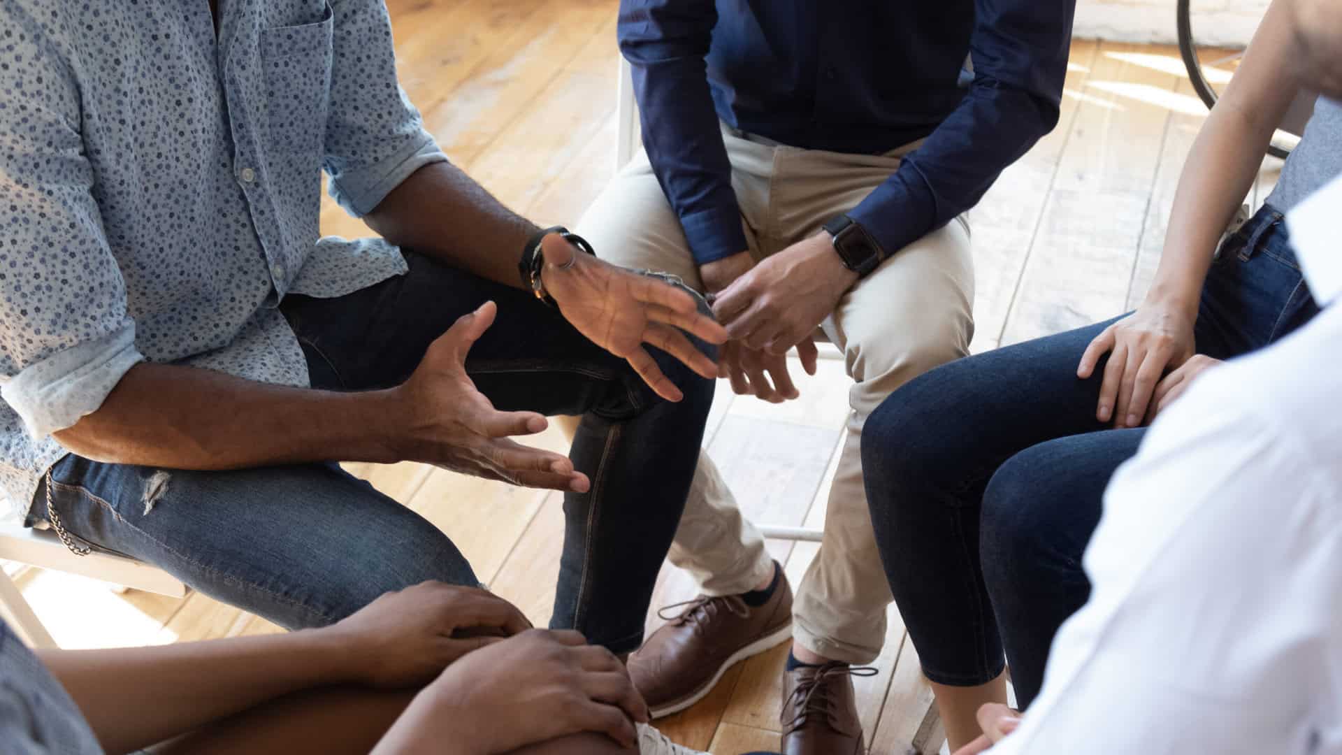 People sitting in a circle, wearing casual clothes, engaged in discussion.