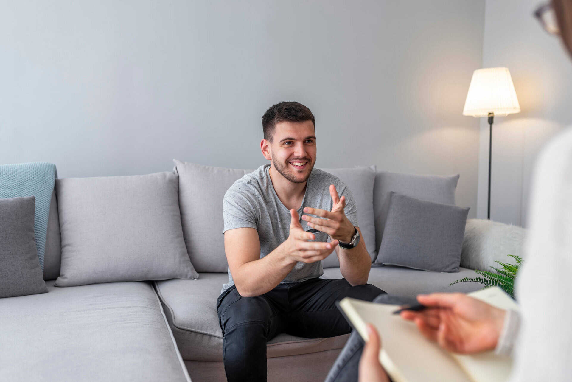 Person wearing a gray t-shirt sitting on a sofa and gesturing.