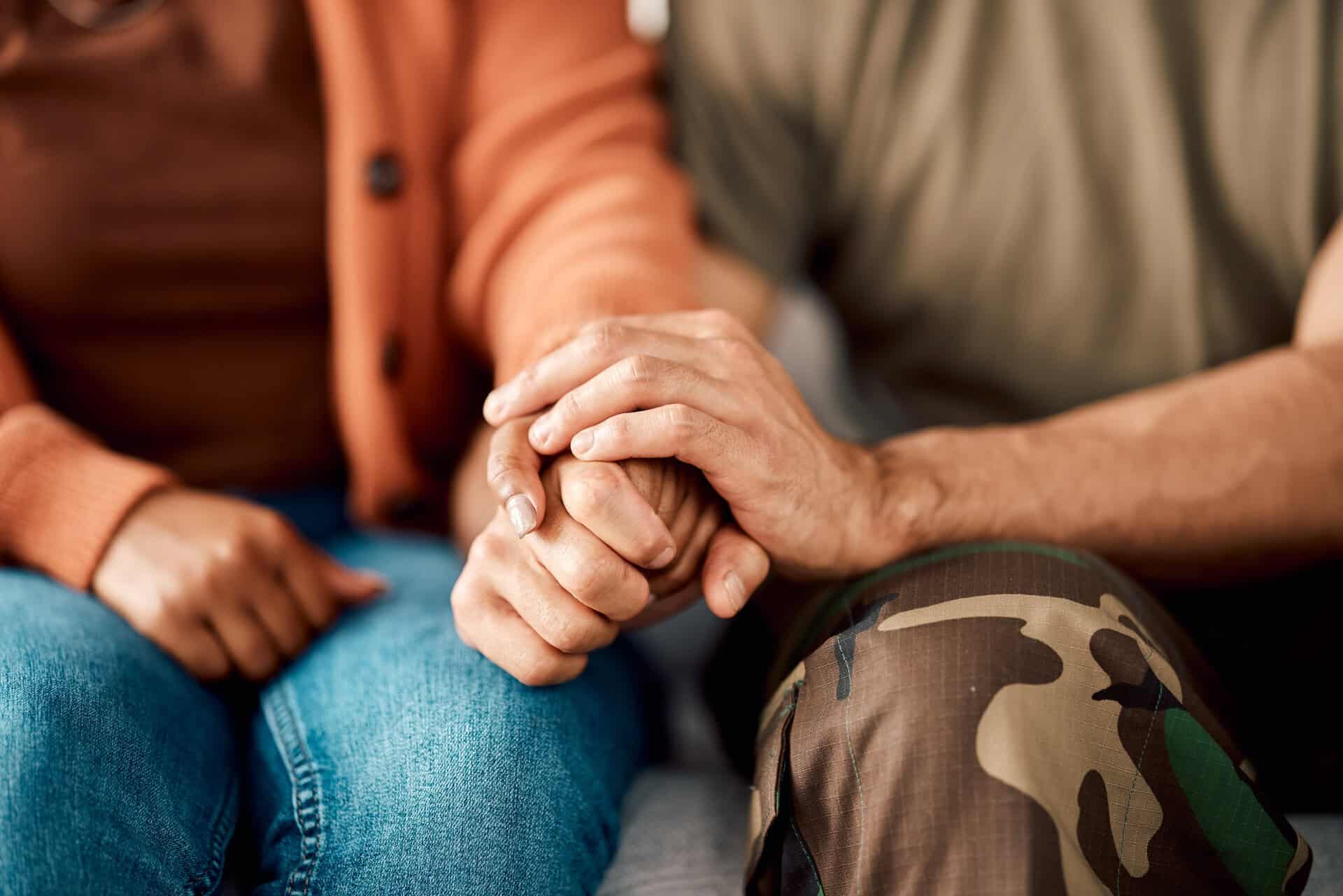 Two people holding hands, one in orange cardigan, one in camouflage pants.