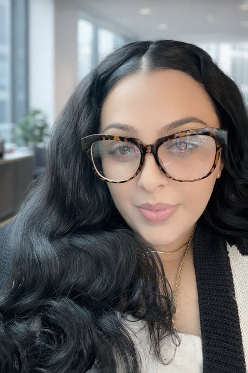 Person with long wavy hair, wearing tortoiseshell glasses and a black and white sweater.