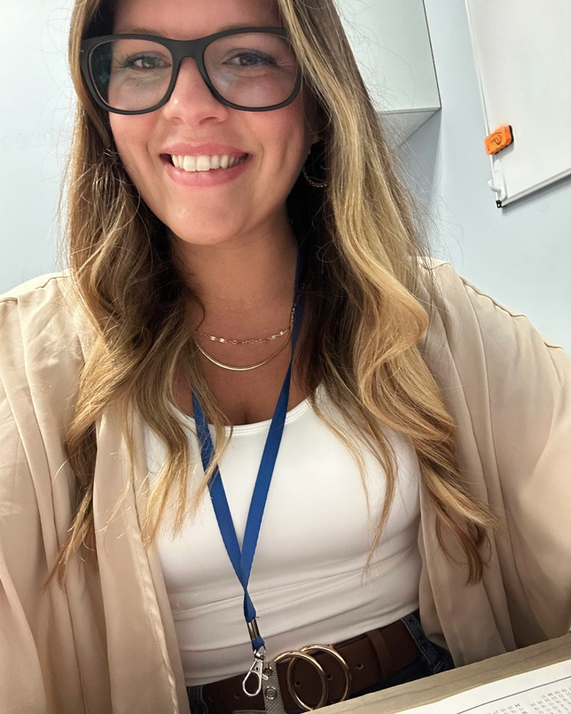 Person wearing glasses, white top, and blue lanyard, smiling.