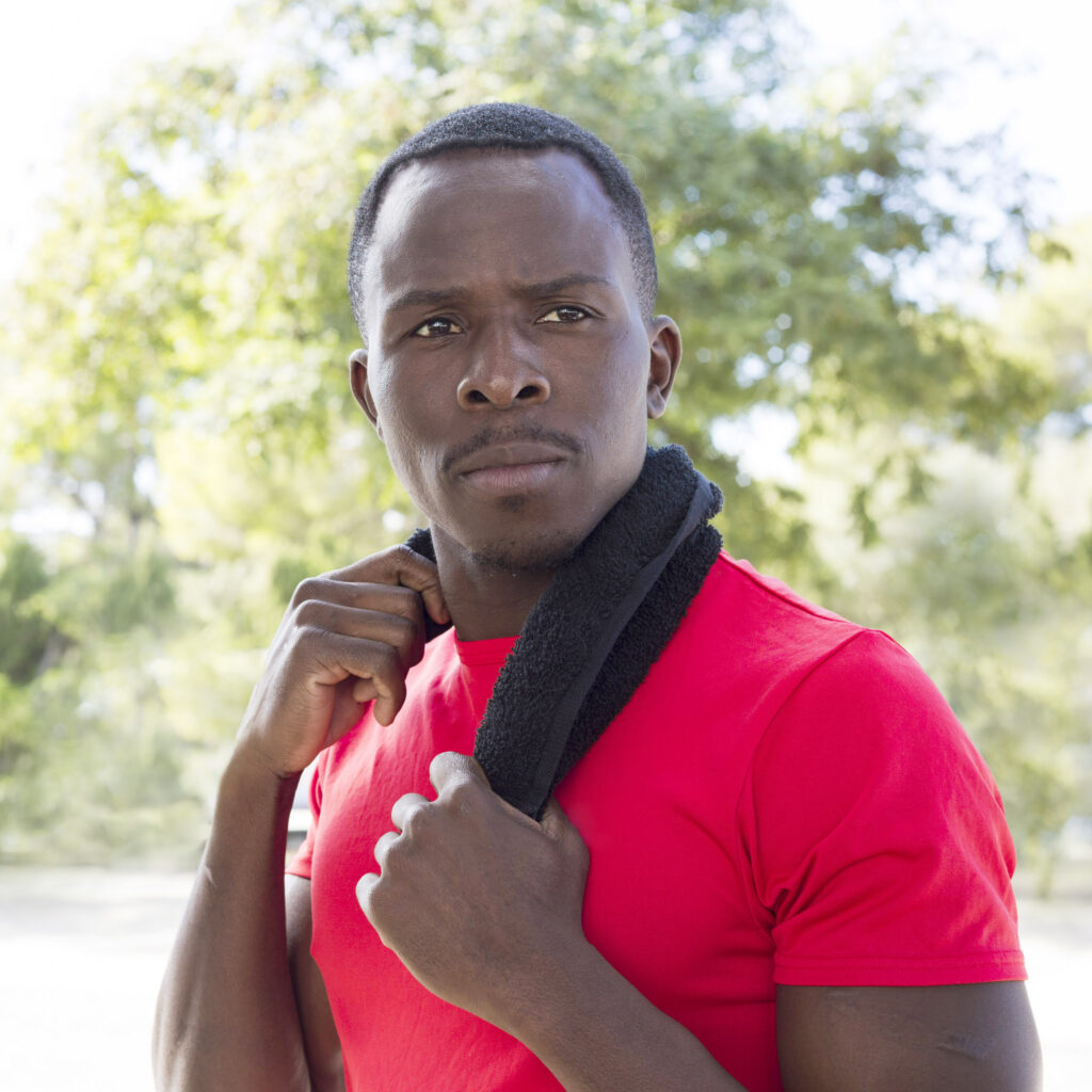 Person in red shirt holding towel around neck outdoors.